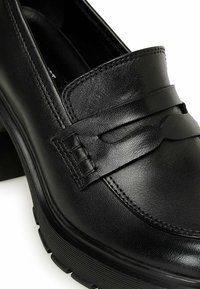 Czarne skórzane mokasyny o gładkiej fakturze, z przeszywanym wzorem i dekoracyjną taśmą na górze. Gumowa podeszwa zapewnia przyczepność.