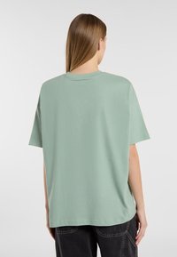 T-shirt oversize vert menthe avec un col rond, des manches courtes et une texture en coton doux. Présenté de dos, sans motifs ni accents.