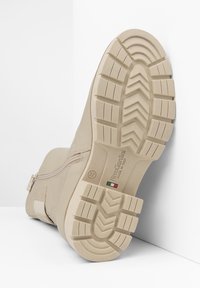 Bottine beige avec une semelle en caoutchouc texturée à motif de semelles, fermeture éclair sur le côté et détails en métal, fabriquée en cuir lisse.
