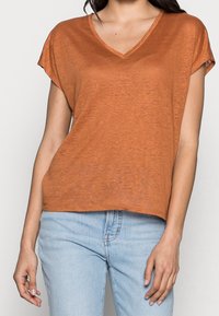 V-ringad, lös t-shirt i varm orange. Tyget har en mjuk, texturerad yta. Korta ärmar och en avslappnad silhuett. Matchas med ljusblå jeans.