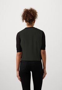 Green cropped vest with structured fabric, black mesh sleeves, and a plain back. Features a round neckline and fitted silhouette.