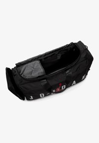 Svart duffelbag med en glatt og slitesterk utside. Har fet hvit tekst og en rød logo. Innsiden er foret med grått stoff og har en glidelåslomme.