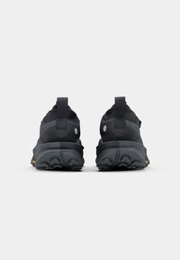 Black athletic shoes with a textured upper, rubber outsoles, and pull tabs at the heel. Features a minimalistic design with reflective accents.