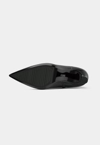 Zapato de tacón alto negro con punta afilada, de cuero liso en la parte superior y suela de goma texturizada con ranuras horizontales. Branding sutil en la plantilla.