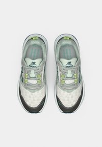 Chaussures de course pour hommes, empeigne en mesh gris clair, superpositions texturées, accents noirs et verts, détails réfléchissants, languette rembourrée et semelle coussinée.