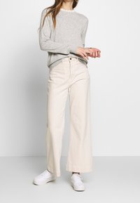 Pull en tricot gris clair avec un col festonné, associé à un pantalon large crème à taille haute et des baskets blanches.