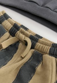 Primo piano di pantaloni con vita elasticizzata a strisce beige e grigio scuro, con un laccio legato, accanto a tessuti piegati di colore grigio scuro a costine.
