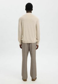 Pull en tricot beige clair avec un col rond, associé à un pantalon gris évasé. Texture douce et subtils détails de design au dos visibles.