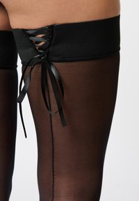 Calze nere sopra il ginocchio caratterizzate da una texture liscia e trasparente, una ampia fascia elastica con dettagli di lacci e nastri in raso.