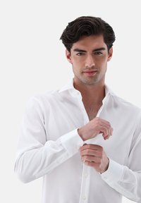 Weißes Baumwollhemd mit klassischem Kragen, durchgehend geknöpft und langen Ärmeln. Auffällige Knopfmanschetten und glatte Textur.