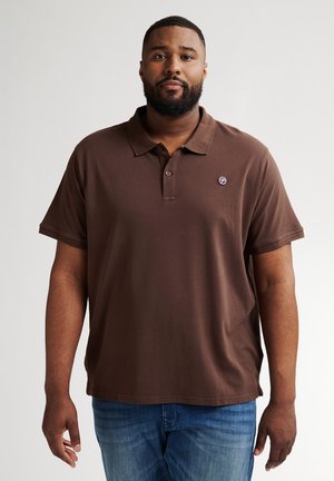 Camisa polo marrón con cuello y tapeta de tres botones, con un pequeño logo en el pecho, combinada con jeans azules.
