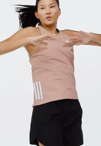 Lichtroze sporttanktop met dunne bandjes en drie witte verticale strepen aan de zijkant, gecombineerd met zwarte shorts. Gladde stoftextuur.