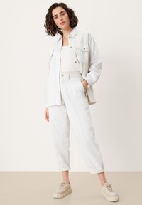 Chaqueta de mezclilla blanca sobre una camiseta de tirantes blanca con canalé y pantalones plisados blancos, combinados con zapatillas de deporte beige claro con suelas gruesas.
