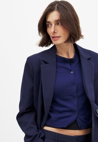 Navy blazer and cardigan set, featuring a smooth fabric texture, button closures, and a tailored fit. Blazer has wide lapels and structured shoulders.