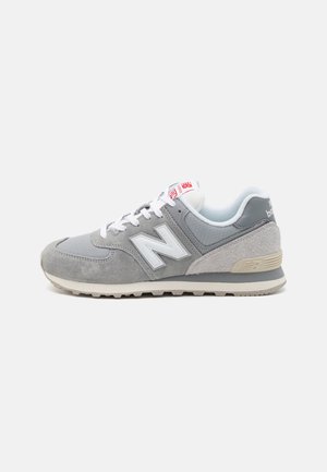 Basket New Balance gris et blanc avec des panneaux en daim et en mesh, des lacets blancs et une semelle texturée sur un fond clair uni.