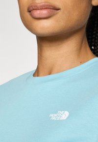 Svijetloplava pamučna majica s okruglim izrezom, sa bijelim izvezenim logotipom The North Face na lijevoj strani prsnog koša.