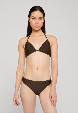 Kobieta o długich ciemnych włosach ubrana w ciemnobrązowy trójkątny top bikini oraz pasujące majtki bikini, stojąca na tle jednolitego, jasnoszarego tła.