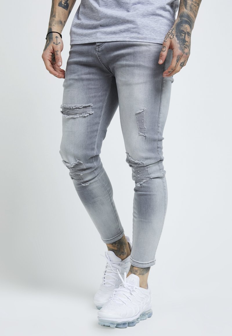 Grå denim slim jeans med slitna detaljer och revor, kombinerat med vita träningsskor. Slät textur med en åtsittande silhuett.