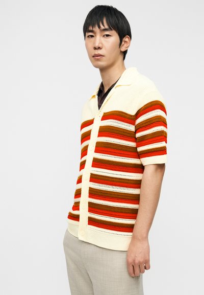 Πλεκτή ζακέτα με κοντά μανίκια και οριζόντιες ρίγες σε εκρού, πορτοκαλί, καφέ και κόκκινο. Ελαφριά, με γιακά και κλείσιμο με κουμπιά.