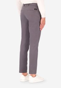 Pantaloni grigi in cotone con una vestibilità slim, dotati di due tasche posteriori e una piccola etichetta con logo sulla vita, abbinati a sneakers bianche.