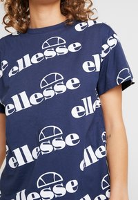 Navy cotton t-shirt featuring large white "ellesse" logo in various orientations. Short sleeves and standard fit with a smooth texture.