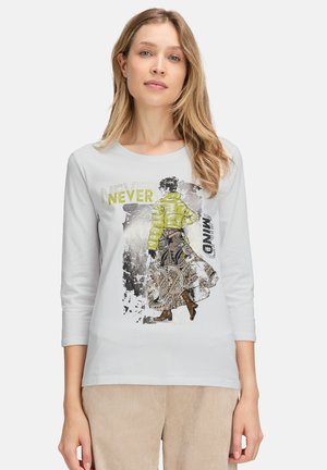 Witte lange mouwen T-shirt met een kleurrijke grafische print van een figuur in een gele jas en een patroonrok, met de tekst "NEVER MIND."