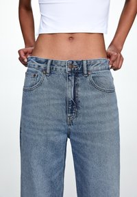 Jeans de mezclilla de color azul claro, de cintura alta y ajuste recto. Presentan un diseño de cinco bolsillos, cierre de botón y áreas sutilmente desgastadas en la tela.