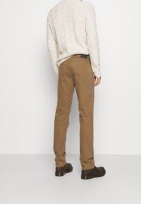 Lichtbruine chinos met een rechte pasvorm en achterzakken, gecombineerd met een gestructureerde crème trui en donkerbruine schoenen.