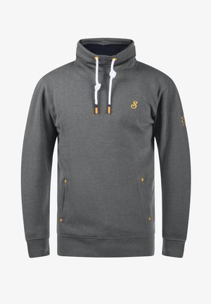 Szürke pulóver magas nyakú, fehér zsinórokkal, narancssárga fém részletekkel és oldalsó zsebekkel. Jellemzője egy kis logó a mellkasán.