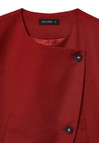 Giacca rossa aderente realizzata in tessuto liscio. Presenta un collo rotondo, una pattina diagonale e un accentuato bottone nero singolo. Etichetta: CALLIOPE.