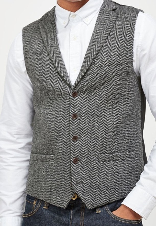 Gilet grigio con motivo a spina di pesce, colletto a lancia, cinque bottoni marroni e due tasche frontali, abbinato a una camicia bianca.