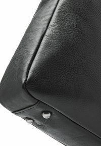 Zwarte leren tas met een gestructureerd oppervlak, rechthoekige vorm en metalen studs aan de onderkant voor versterking.