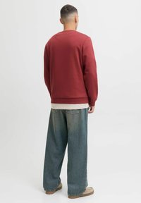 Bordeaux sweatshirt met een ronde hals, geribbelde manchetten en zoom. Gecombineerd met loszittende lichtblauwe jeans en beige schoenen.