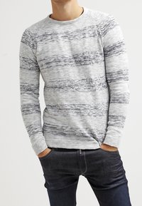 Grau gestrickter Pullover mit horizontalen schwarzen Streifen, Rundhalsausschnitt und langen Ärmeln, kombiniert mit dunklen Jeans.