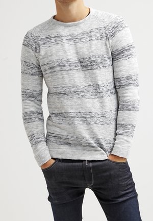 Grå stickad tröja med horisontella svarta ränder, rund halsringning och långa ärmar, i kombination med mörka jeans.