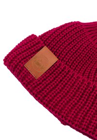 Czerwona, dziana czapka z zakładanym rondem, z brązową skórzaną naszywką z wytłoczonym logotypem. Teksturalny wzór z wyraźnymi detalami szwów.