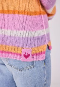 Strickpullover mit rosa, lila, orange und weißen Streifen; hat ein rosa Etikett mit einem Herz-Logo am Saum; weiche Textur.
