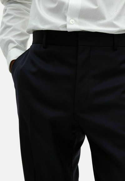 Dunkelblaue, taillierte Hose mit glatter Textur, ausgestattet mit Seitentaschen und Gürtelschlaufen, kombiniert mit einem weiß gestreiften Hemd.