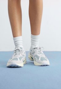 Light gray sneakers with green accents, mesh and suede materials, lace-up design, round toe, and textured sole, paired with white ribbed socks.