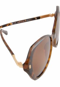 Lunettes de soleil en écaille de tortue avec verres marron. Monture carrée arrondie, accents en métal doré et charnières flexibles. Fabriquées en Chine.
