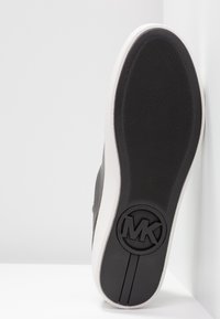 Semelle d'une basket Michael Kors noire et blanche avec une adhérence texturée et le logo MK embossé près du talon.