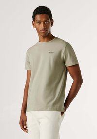 T-shirt en coton vert olive avec col rond, manches courtes et petit logo sur la poitrine. Texture lisse et coupe décontractée.