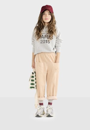 Lichtgrijze sweatshirt met Parijs 2015-print, beige corduroy broek met grote zakken, bordeauxrode pet en grijze sneakers met witte accenten.