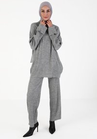 Grauer gerippter Strickpullover und Hosenanzug mit lockerer Passform, breiten Ärmeln und hohem Kragen, kombiniert mit schwarzen spitzen Pumps.