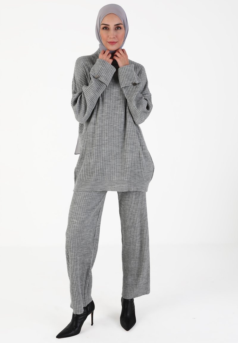 Grauer gerippter Strickpullover und Hosenanzug mit lockerer Passform, breiten Ärmeln und hohem Kragen, kombiniert mit schwarzen spitzen Pumps.