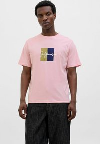Rosa kortærmet t-shirt med et firkantet grafisk design i farverne beige, marineblå og hvid. Lavet af blødt stof med en afslappet pasform.