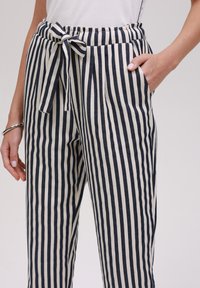 Pantalons rayés en crème et bleu marine, avec une taille élastique ornée d'un nœud, deux poches latérales et une coupe décontractée.