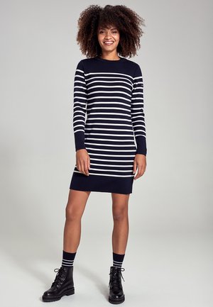 Abito a righe blu navy con maniche lunghe, caratterizzato da strisce orizzontali bianche. Indossato con stivali da combattimento neri e calze a righe.