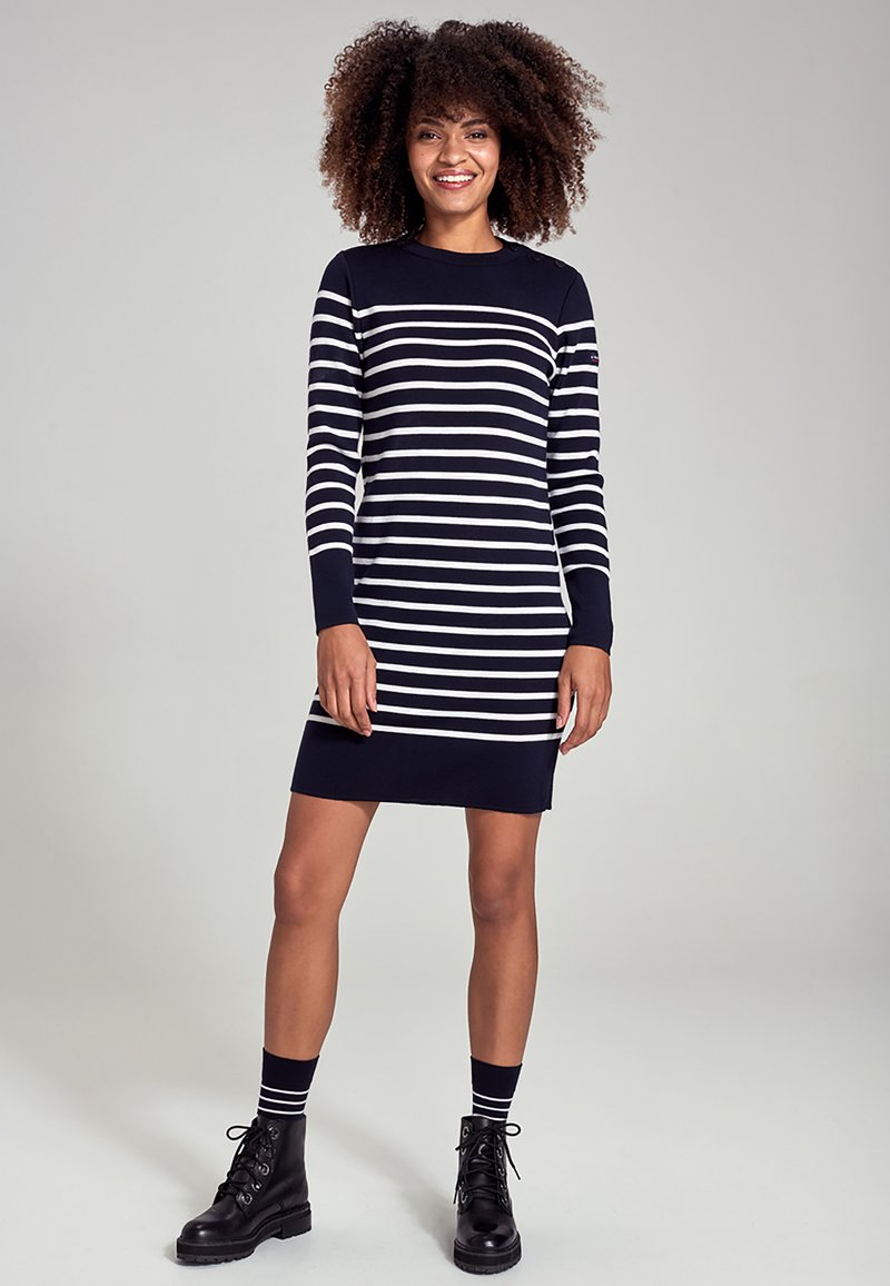 Robe rayée bleu marine avec des manches longues, dotée de rayures blanches horizontales. Portée avec des bottes de combat noires et des chaussettes rayées.