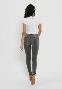 Gray skinny jeans with a high waist, featuring back pockets and a smooth fabric texture. Paired with a white ribbed short-sleeve top.